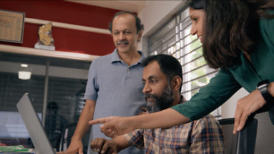 Een groep mensen zit rond een computerscherm in een gedimd verlicht kantoor.