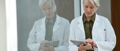 Healthcare professionals in lab coats using tablets indoors.