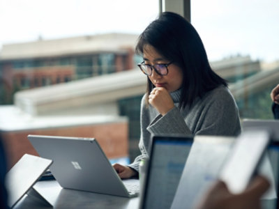 Person working on a laptop at a table during a meeting, with other laptops visible nearby