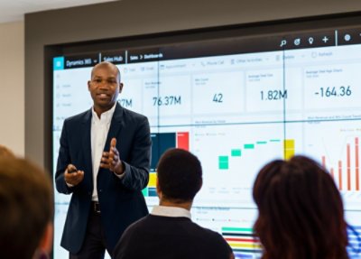 Person presenting Dynamics 365 sales dashboard insights on a large screen to team members in a meeting room