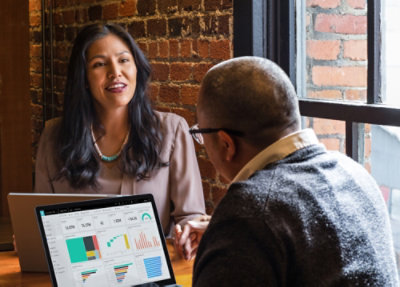 Two people reviewing Dynamics 365 sales data on laptop during a business meeting near a window
