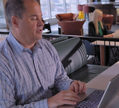 Person using a laptop in a modern workspace with seating area in the background.