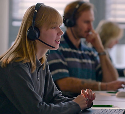 Person wearing a headset working on a laptop in an office environment.