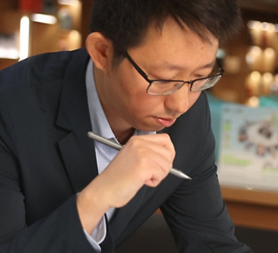 Person writing on a tablet or device using a stylus in an indoor setting.