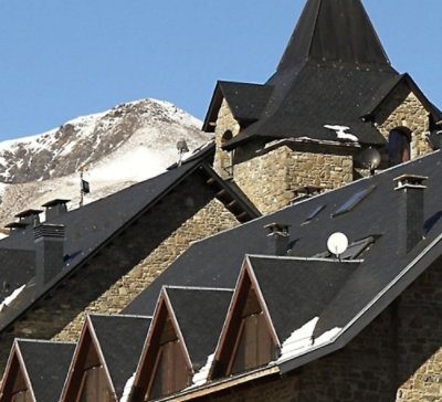 Mountain village with stone buildings and snow‑covered peaks in the background.
