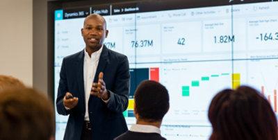 Person presenting Dynamics 365 sales dashboard insights on a large screen to team members in a meeting room