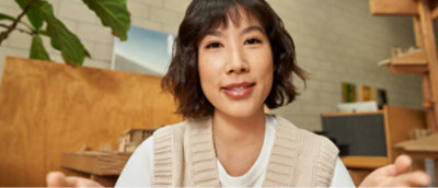 Seorang wanita berambut hitam pendek dan mengenakan rompi sweter putih tersenyum ke kamera.