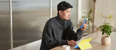 Person checking a mobile phone while using a tablet at a table.
