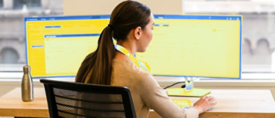 Person working at a desk with dual monitors displaying yellow interfaces.