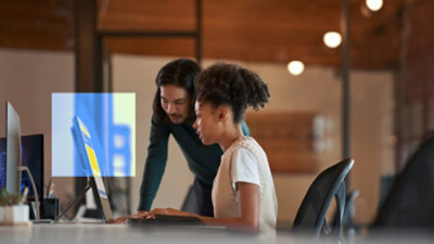 Two coworkers collaborating at a desktop computer in a modern office.