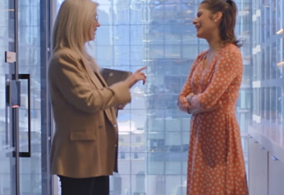 A woman in a brown jacket talking to another woman.