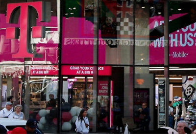 A woman walking past a store with a large glass window, a pink sign, and balloons visible inside.