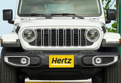 A close-up of the front of a white car showing its grill with the text Hertz.