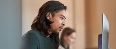 A person with long hair wearing a green shirt, looking away, with a blurry background.