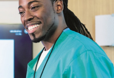 A person is wearing teal medical scrubs, he has a bright smile.
