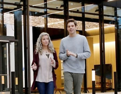  Two coworkers walking and talking inside a modern office building.