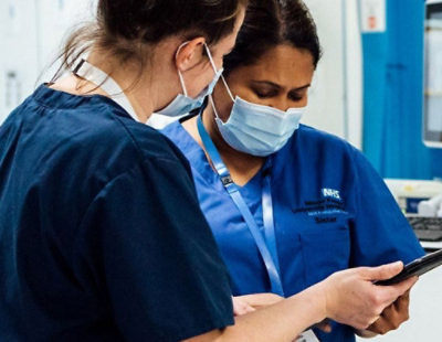 Healthcare workers wearing masks reviewing information on a tablet in a clinical setting.