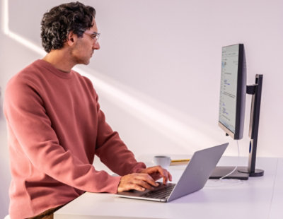 Person working on a laptop at a standing desk with an external monitor.