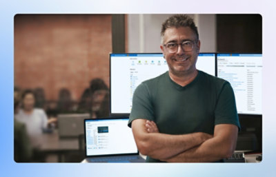 Person standing with arms crossed in front of multiple computer monitors in an office.