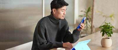 Person using a smartphone and tablet at a desk with indoor plants.