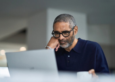 A man wearing glasses and a blue shirt looks at a laptop.