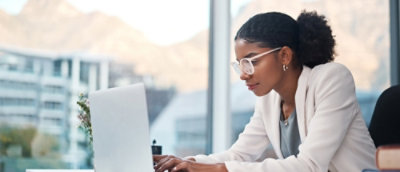 A woman wearing glasses and a white jacket is working on a computer.