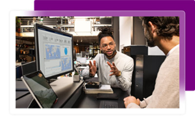 Two men sitting and talking infront of a computer screen
