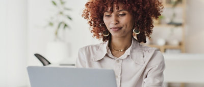 A person with curly hair sits at a desk, focused on a laptop.