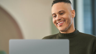 Person smiling and looking at a laptop screen indoors.