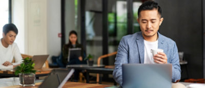 Person works on a laptop while holding a cup in a shared workspace.