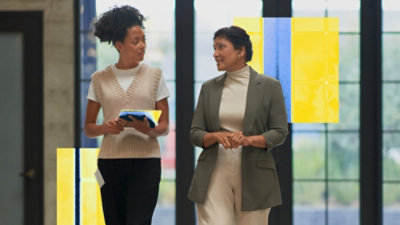 Two coworkers walking and talking, holding a tablet.