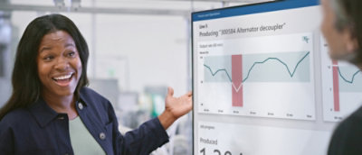 Woman standing next to a monitor screen.