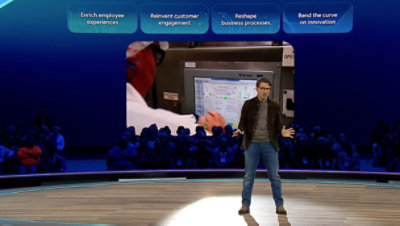 A man standing at a podium, in the background a video is displayed on the screen.
