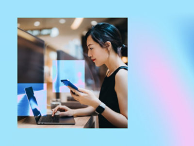 A women holding a mobile and working on a laptop.