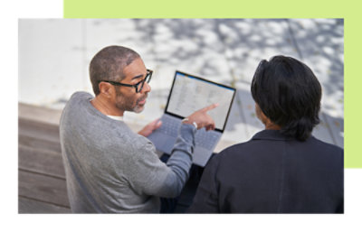 Two people reviewing information on a laptop outdoors.