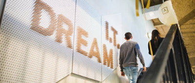 A man in a grey sweater walking down a staircase with a sign that reads L.T. DREAM.