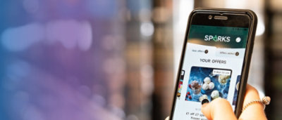 A close-up of a phone displaying the text SPARKS YOUR OFFERS.