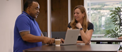 A man and woman sitting at a table with a laptop.