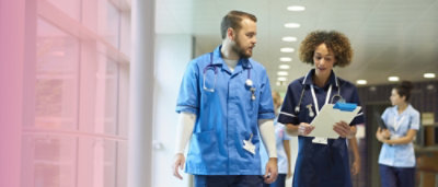 A man and woman wearing scrubs, with the woman holding a clipboard.