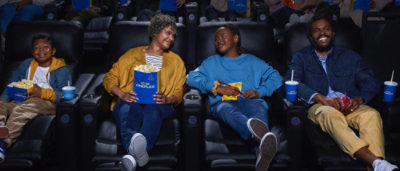 A man and woman sitting in a theater holding a blue container of popcorn.