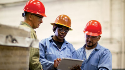 A group of people wearing hard hats looking at a tablet.