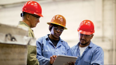 Three people wearing saftey hats and looking at a tablet.