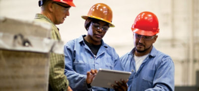 Three people wearing saftey hats and looking at a tablet.