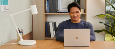 A desk with a laptop, white lamp, and a small square on a white wall nearby.