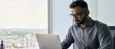 Person working on a laptop at a desk near a window with a city view.