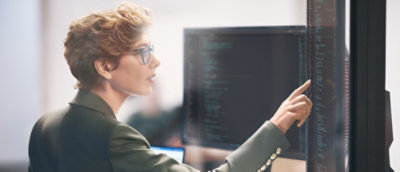 Person interacting with a large monitor displaying lines of code in a work environment.