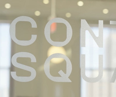 Frosted glass office wall with partial text reading “CONSQUA” visible from inside the workspace.