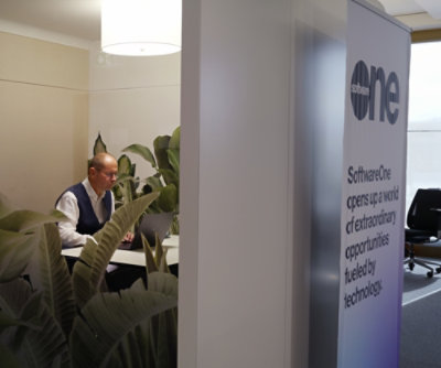 Person working at a desk in a quiet office space separated by glass walls and indoor plants.