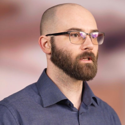 Person speaking on camera in a studio setting while wearing glasses.