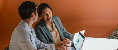 Two colleagues collaborating on a tablet‑style laptop while reviewing content together at a table.